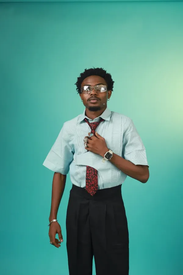 Model in clear-framed glasses and an aqua shirt, holding a red and black tie