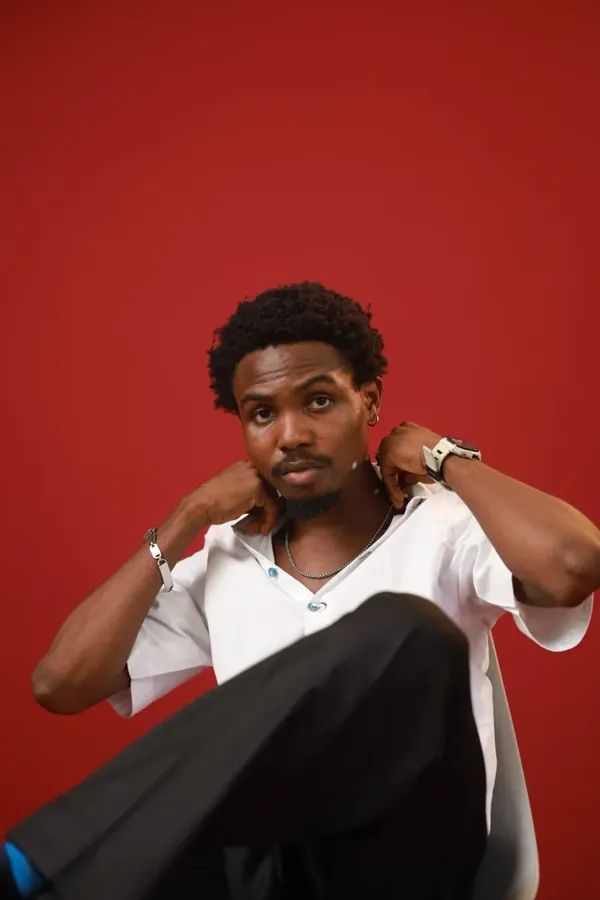 Model seated in the white shirt, adjusting his collar
